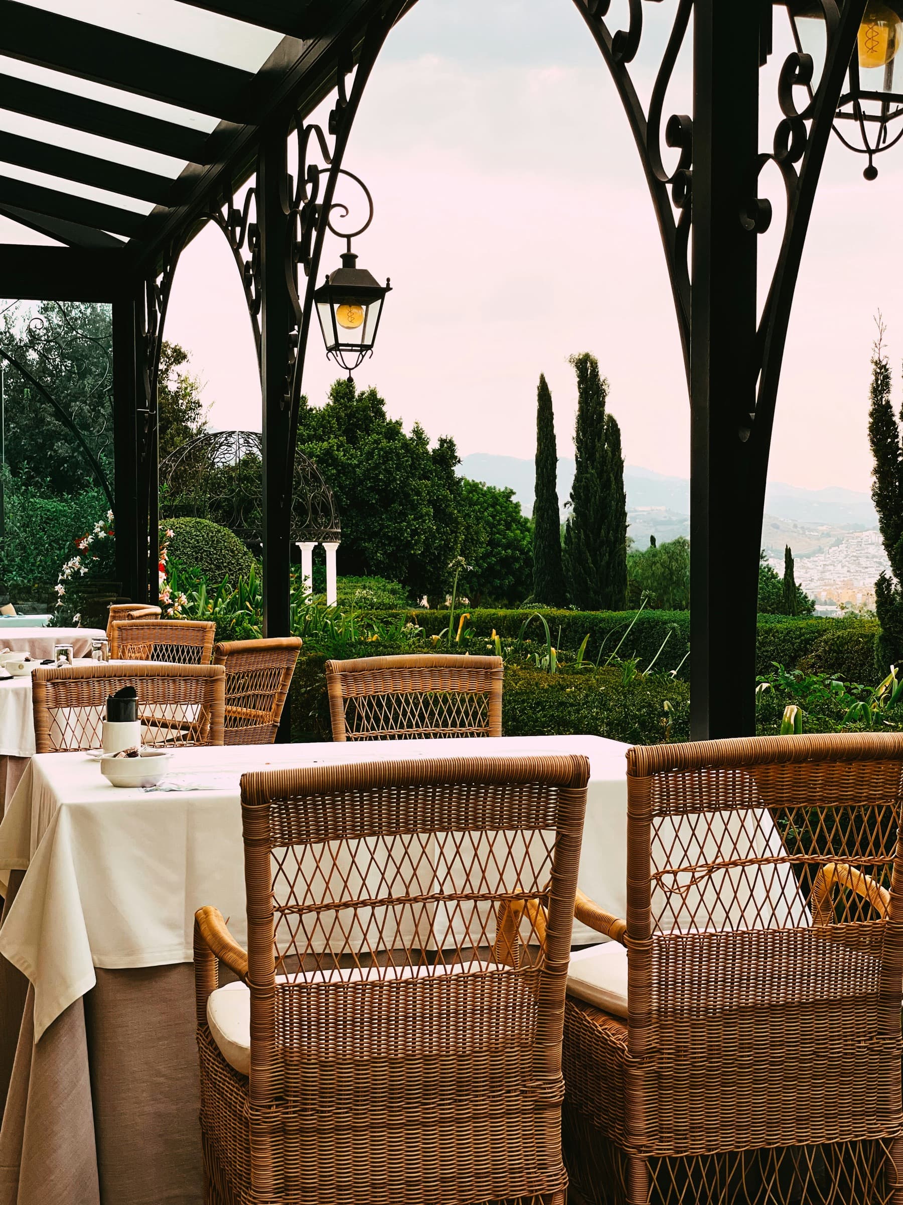 The terrace of a Tuscan hotel laid for breakfast, with cypresses and hills beyond