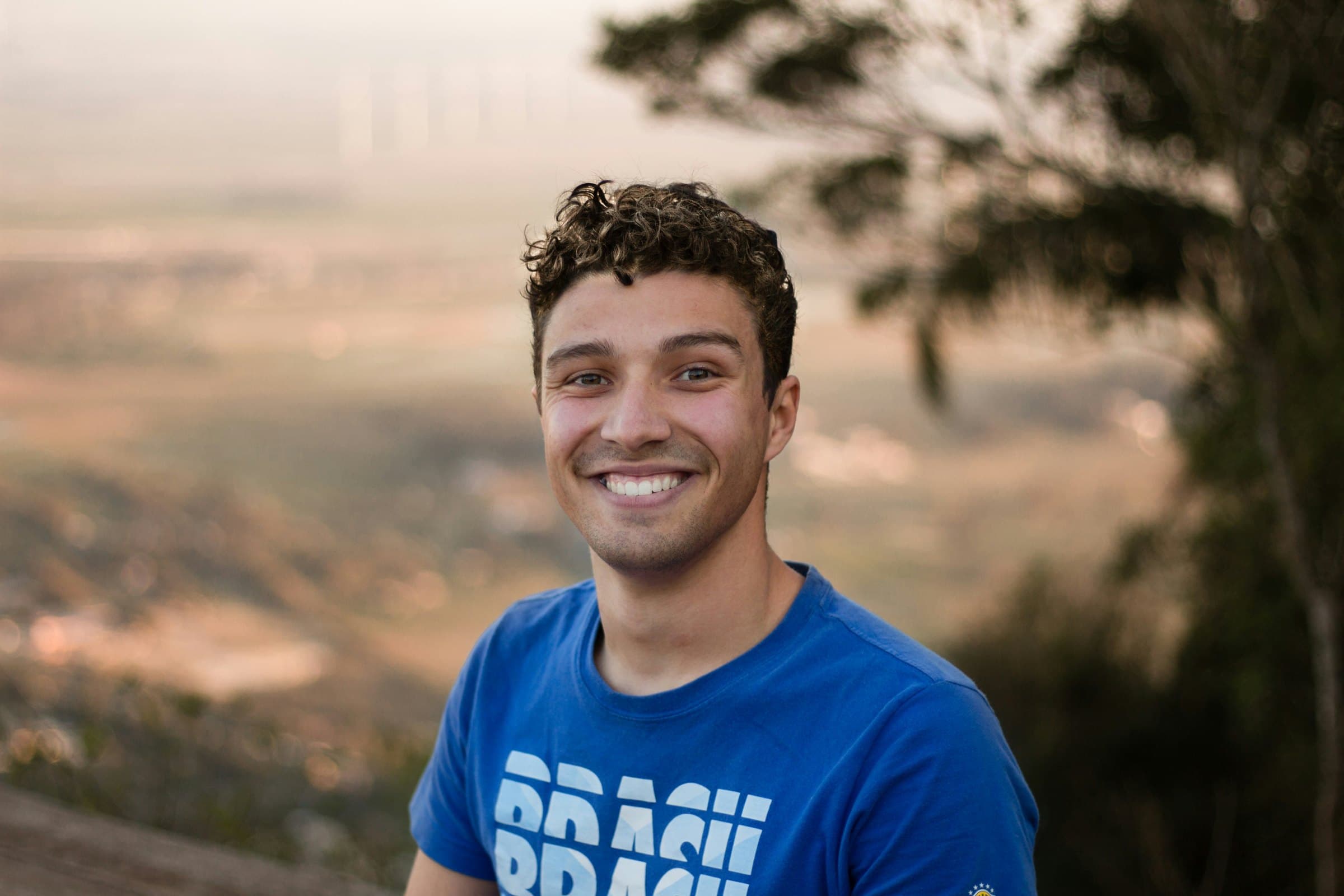 A young professional smiling, a landscape at sunset behind him